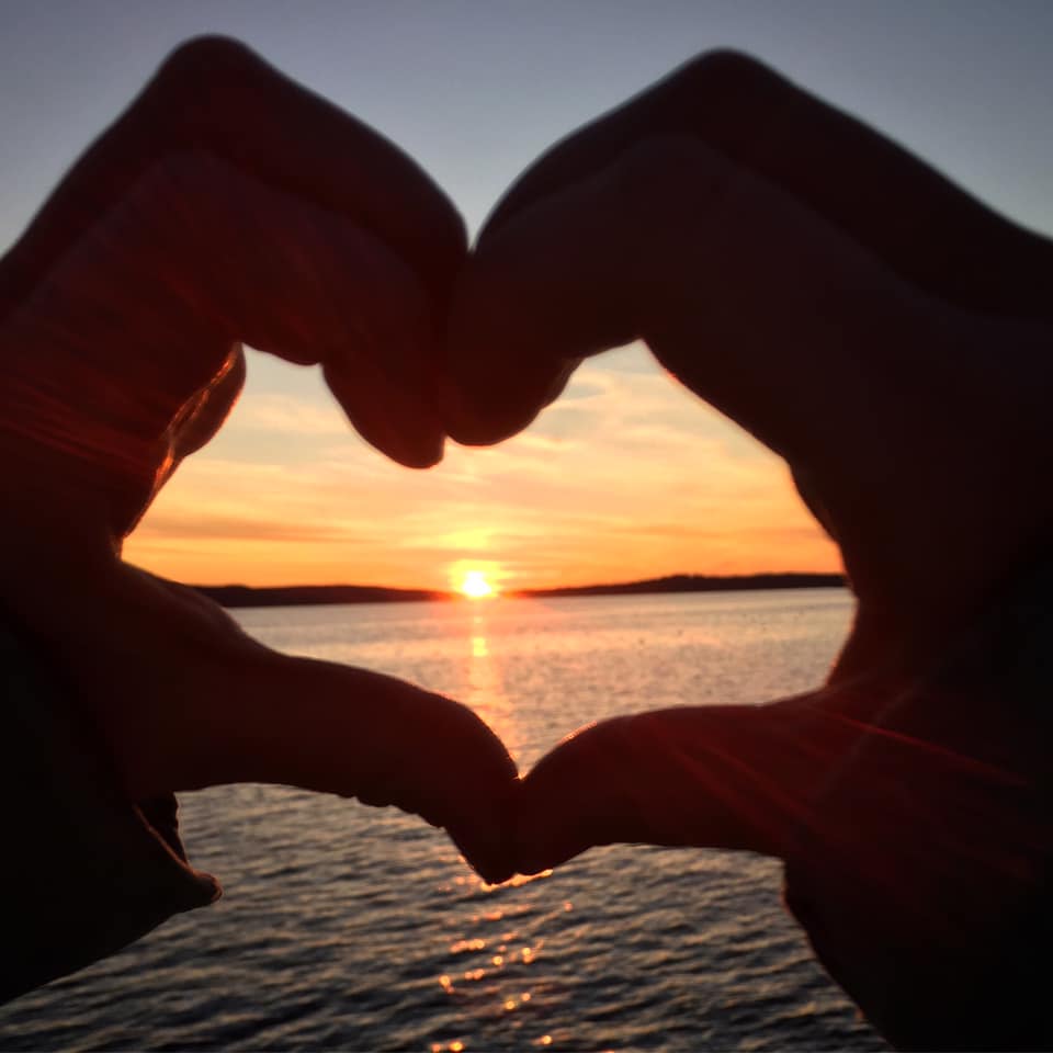 person making a heart with their hands around a sunset